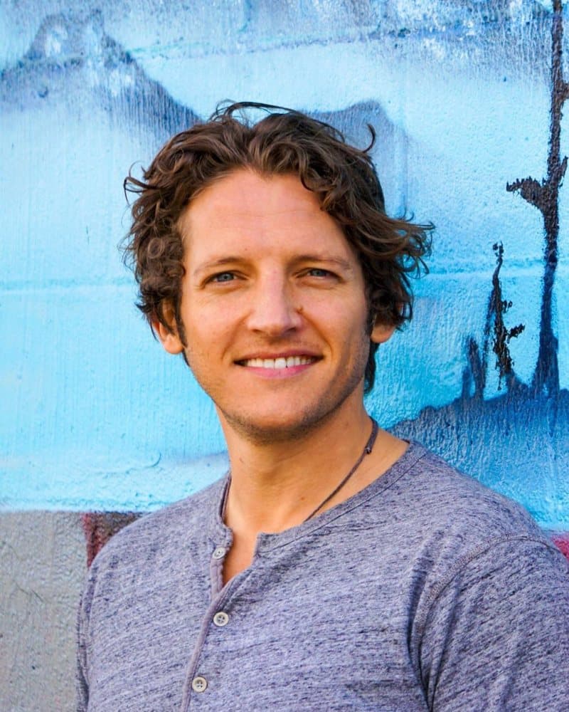 Logan Crowell smiling in front of a blue painted mural